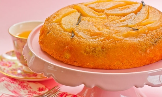 Pear Vanilla Upside Down Cake sitting on white scalloped cake stand with tea & pink background