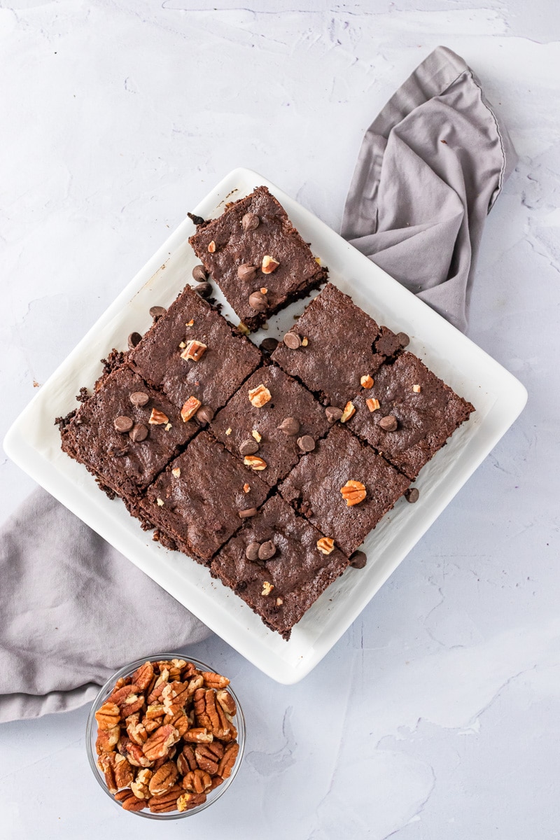 plate full of cut almond flour brownies next to a bowl of nuts