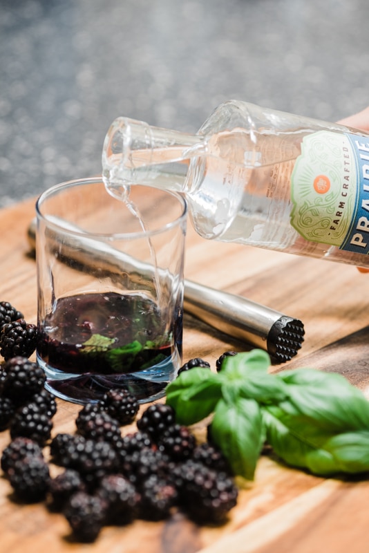 pouring gin over blackberries in a cocktail glass