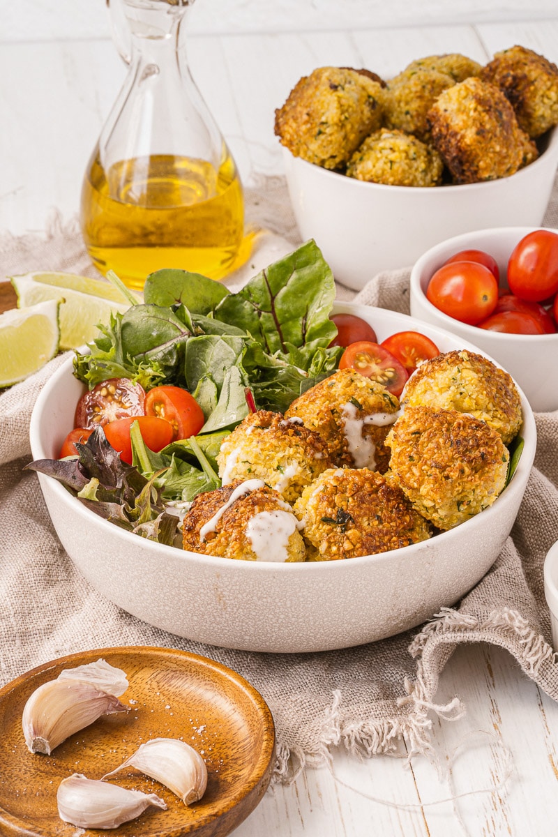falafel bowl on table with condiments and more falafels in bowls
