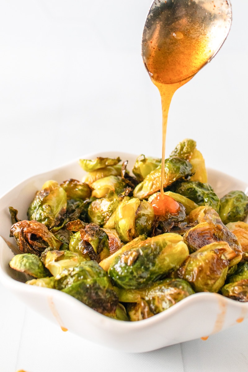 spoonful of honey sriracha sauce drizzling over brussels sprouts