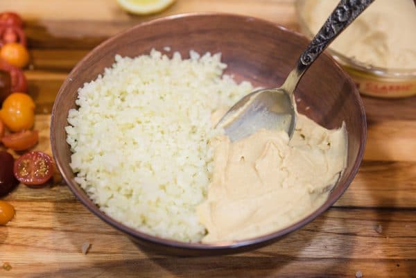 adding riced cauliflower and hummus to a bowl