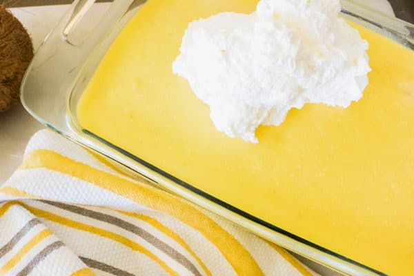 adding whipped cream to pina colada poke cake