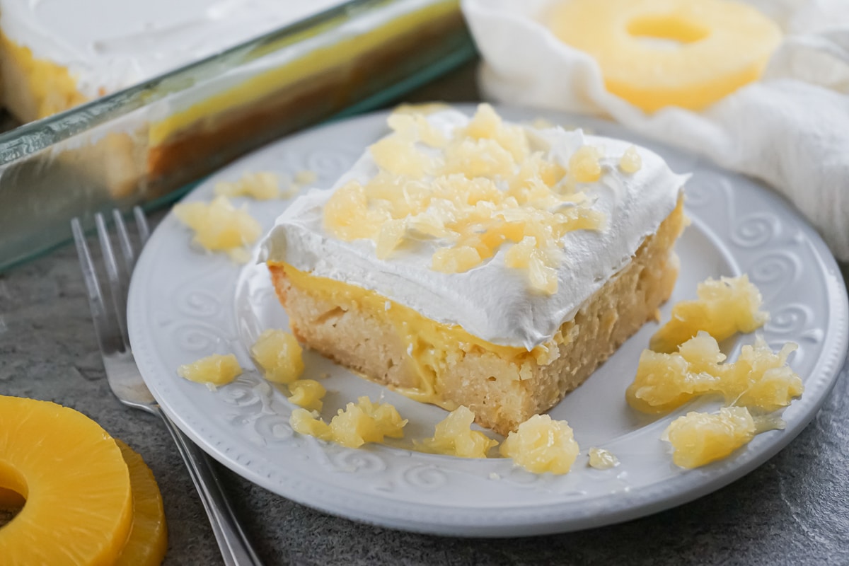 slice of Pineapple Poke Cake on a plate surrounded by crushed pineapple