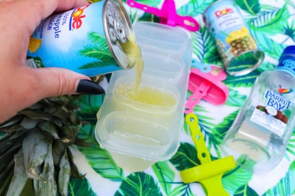 pouring pineapple juice on top of rum in the popsicle molds