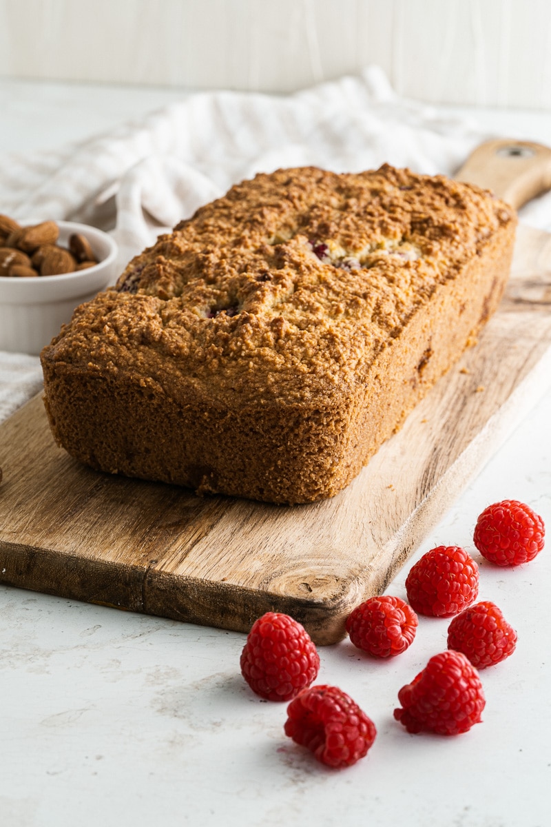 side view loaf of raspberry bread on wooden bread board next to raspberries