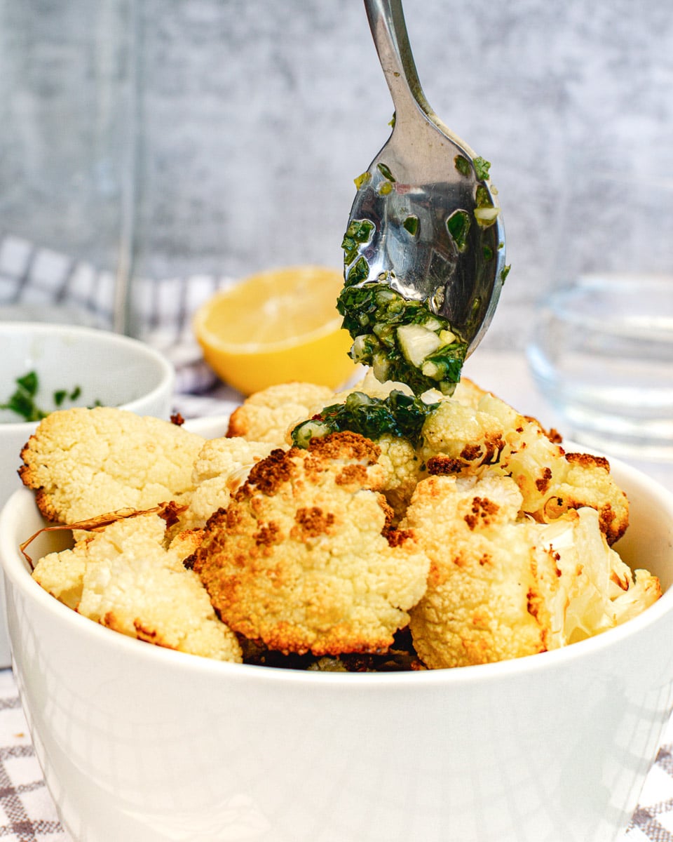 spoon dripping lemon garlic herb sauce over roasted cauliflower in bowl