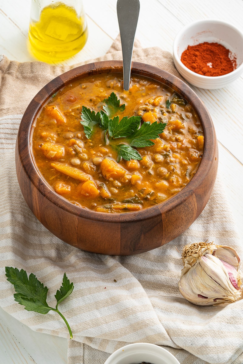 wooden bowl of one-pot sweet potato lentil stew with spoon and sprig of parsley