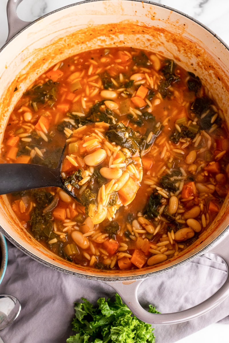 black ladle scooping out tuscan kale soup from pot