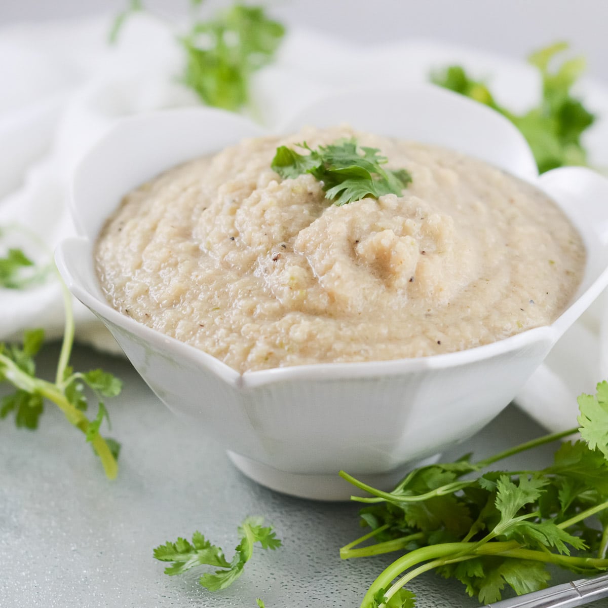 vegan cauliflower soup in a white bowl with fresh herbs on the table