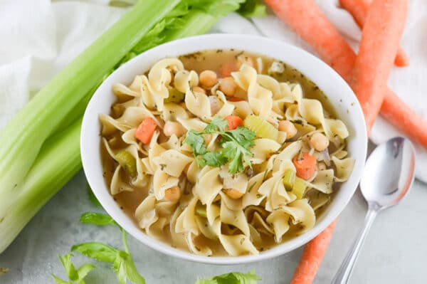 vegan chicken noodle soup with chickpeas on a table with fresh veggies