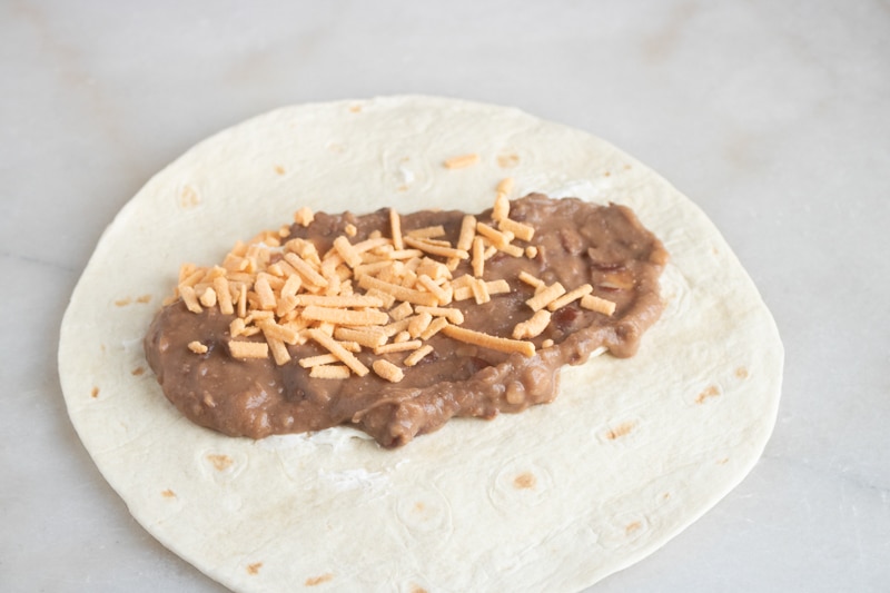 refried beans and vegan cream cheese being added to enchiladas