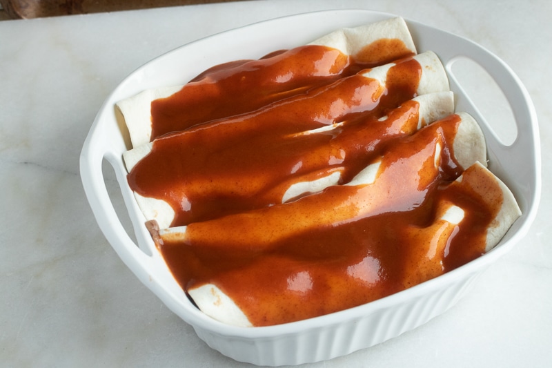 red enchilada sauce being poured over vegan enchiladas