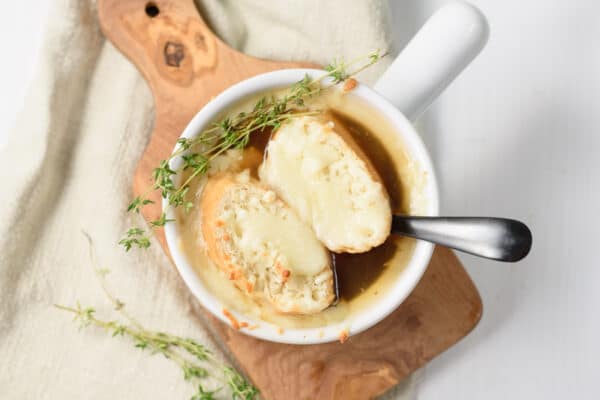 french onion soup being served with a garnish of thyme leaves and topped with dairy free cheese toasts