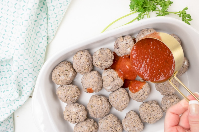 pouring marinara sauce over vegan meatballs