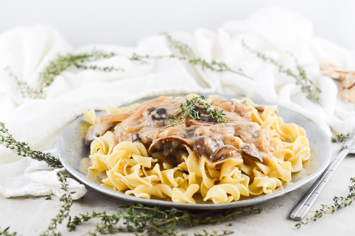 vegan mushroom stroganoff on a table with a white cloth and sprigs of herbs