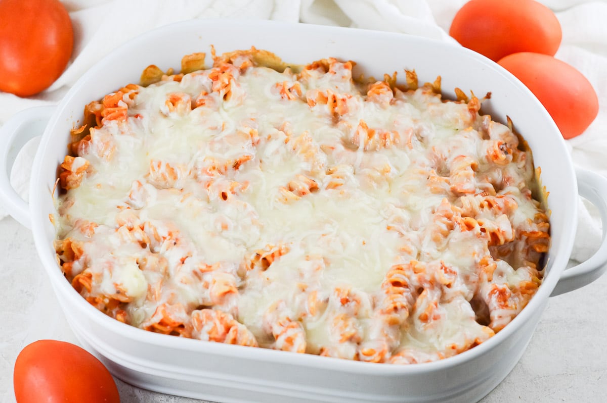 Vegan Pasta Bake in a white dish surrounded by tomatoes