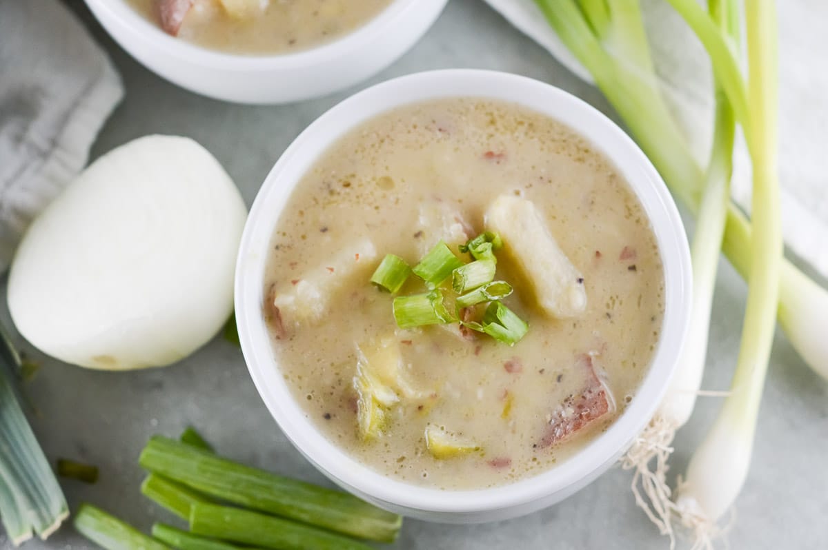 vegan potato leek soup on a table next to onions