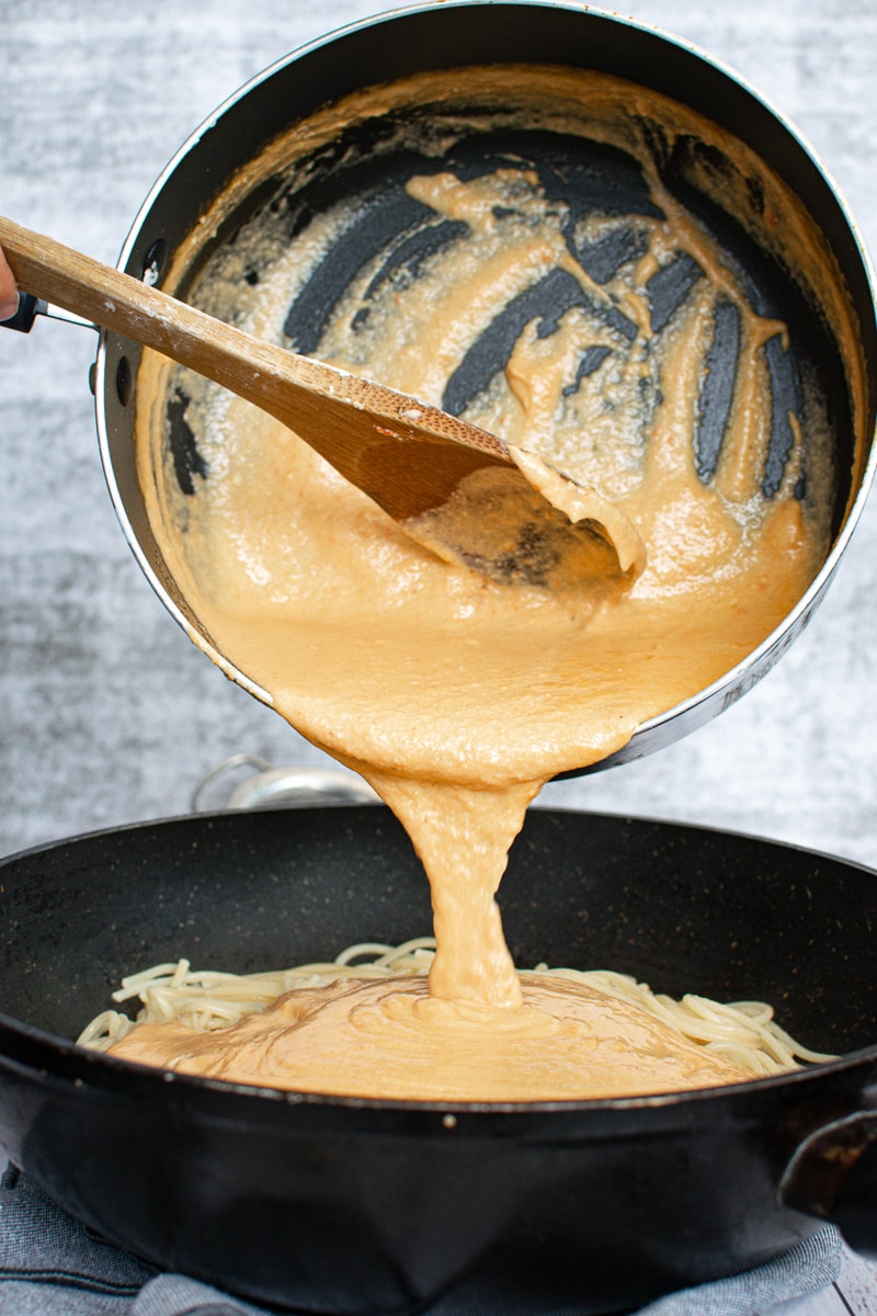 pouring red pepper sauce onto pasta