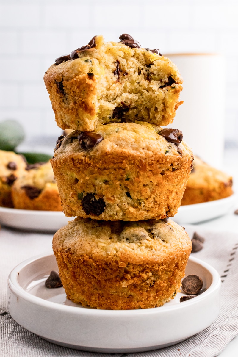 stack of 3 zucchini chocolate chip muffins with a bite taken out of the top one