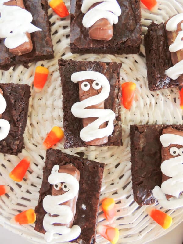 Halloween mummy brownies topped with Twix bars, candy eyes and white icing on a woven tray
