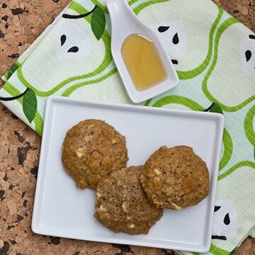 Overhead view of apple cinnamon quinoa oatmeal cookies on a white plate with a small dish of honey