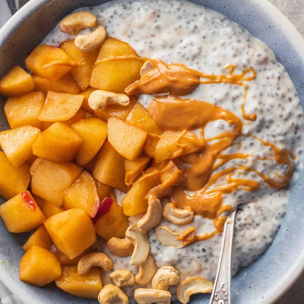 Apple pie coconut chia pudding topped with cinnamon apples, cashews, and peanut butter