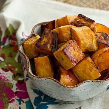 Overhead view of roasted apple cider glazed sweet potatoes in a speckled bowl