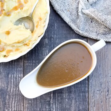 Overhead view of apple cider gravy in a white gravy boat next to a dish of mashed potatoes with fresh thyme