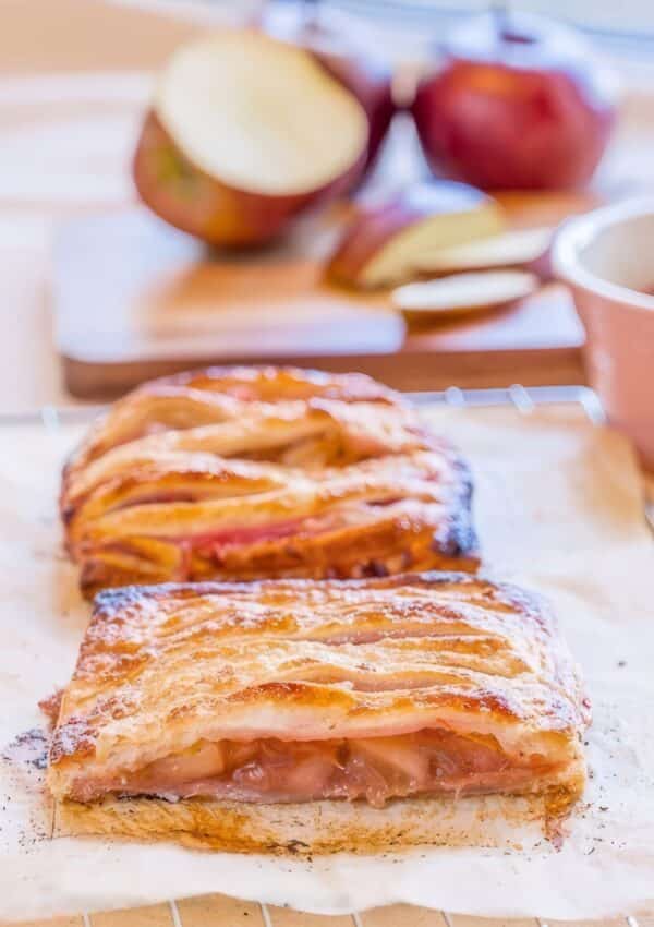 Sliced puff pastry apple rhubarb pie showing the fruit filling, with fresh apples, a knife, and a bowl of rhubarb compote in the background