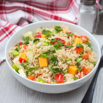 Bowl of brown rice salad with diced apples, red bell peppers, cheddar cheese, and parsley