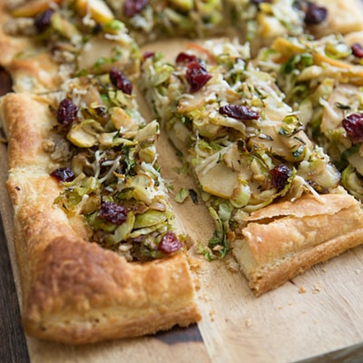 Close-up of Brussels Sprout and Apple Tart with Walnut Pesto and cranberries, sliced on a wooden board