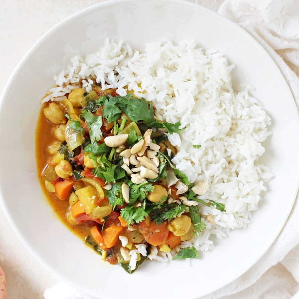 Overhead view of vegetarian apple curry with chickpeas, kale, and cashews served over basmati rice in a white bowl