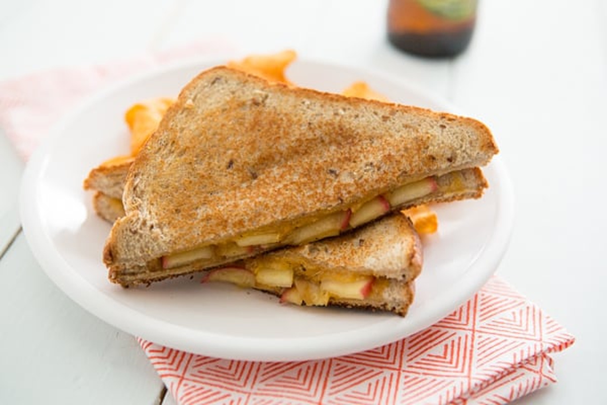 A maple sage apple and cheddar grilled cheese sandwich sliced in half on a plate with sweet potato chips
