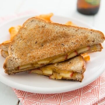 Overhead close-up of a maple sage apple and cheddar grilled cheese sandwich cut in half on a white plate