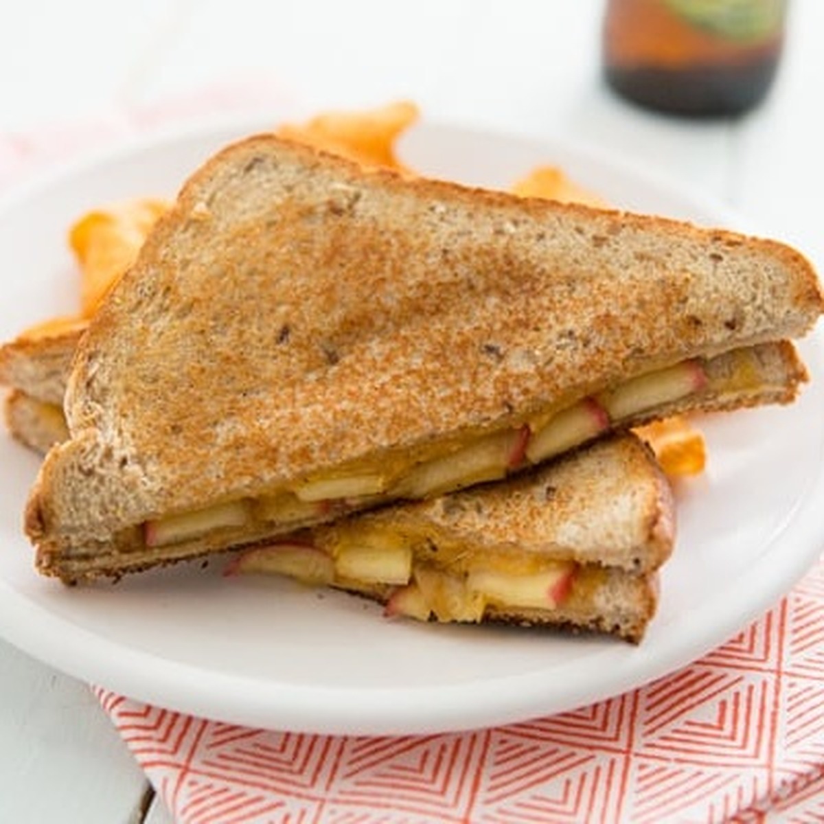 Overhead close-up of a maple sage apple and cheddar grilled cheese sandwich cut in half on a white plate