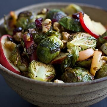 Bowl of roasted brussels sprouts and apples with walnuts, cranberries, and a wooden spoon