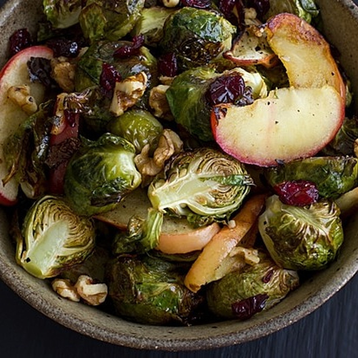 Overhead close-up of roasted brussels sprouts and apples with cranberries and walnuts in a stoneware bowl
