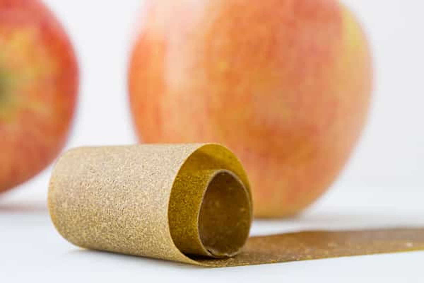 Green apple fruit leather rolled up next to whole apples