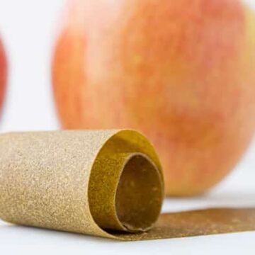 Rolled green apple fruit leather with fresh apples in the background