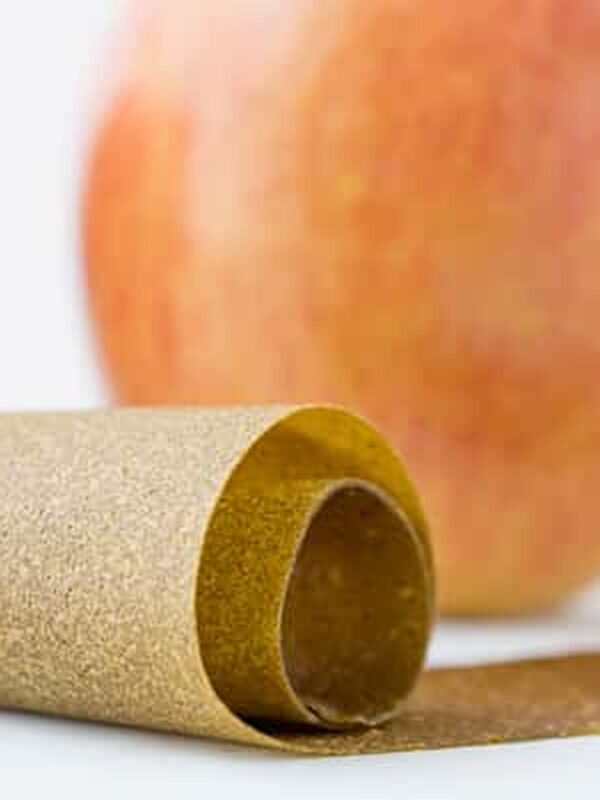 Vertical shot of rolled green apple fruit leather with an apple behind it
