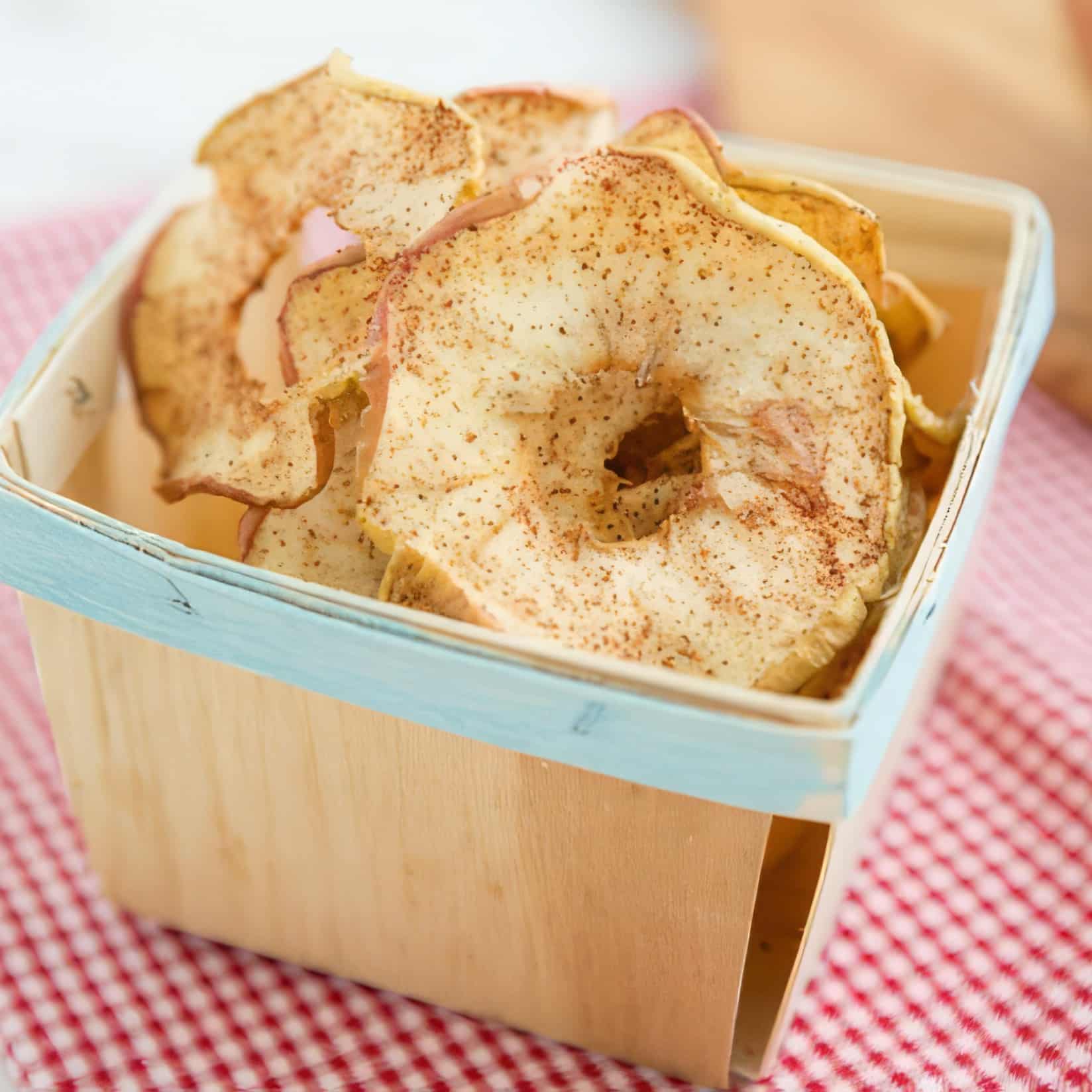 Soft and chewy spiced dried apple rings piled in a wooden berry basket on a red gingham cloth