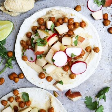 Overhead view of open-faced spiced chickpea tacos topped with crispy roasted chickpeas, diced apple, sliced radish, and cilantro on a baking sheet