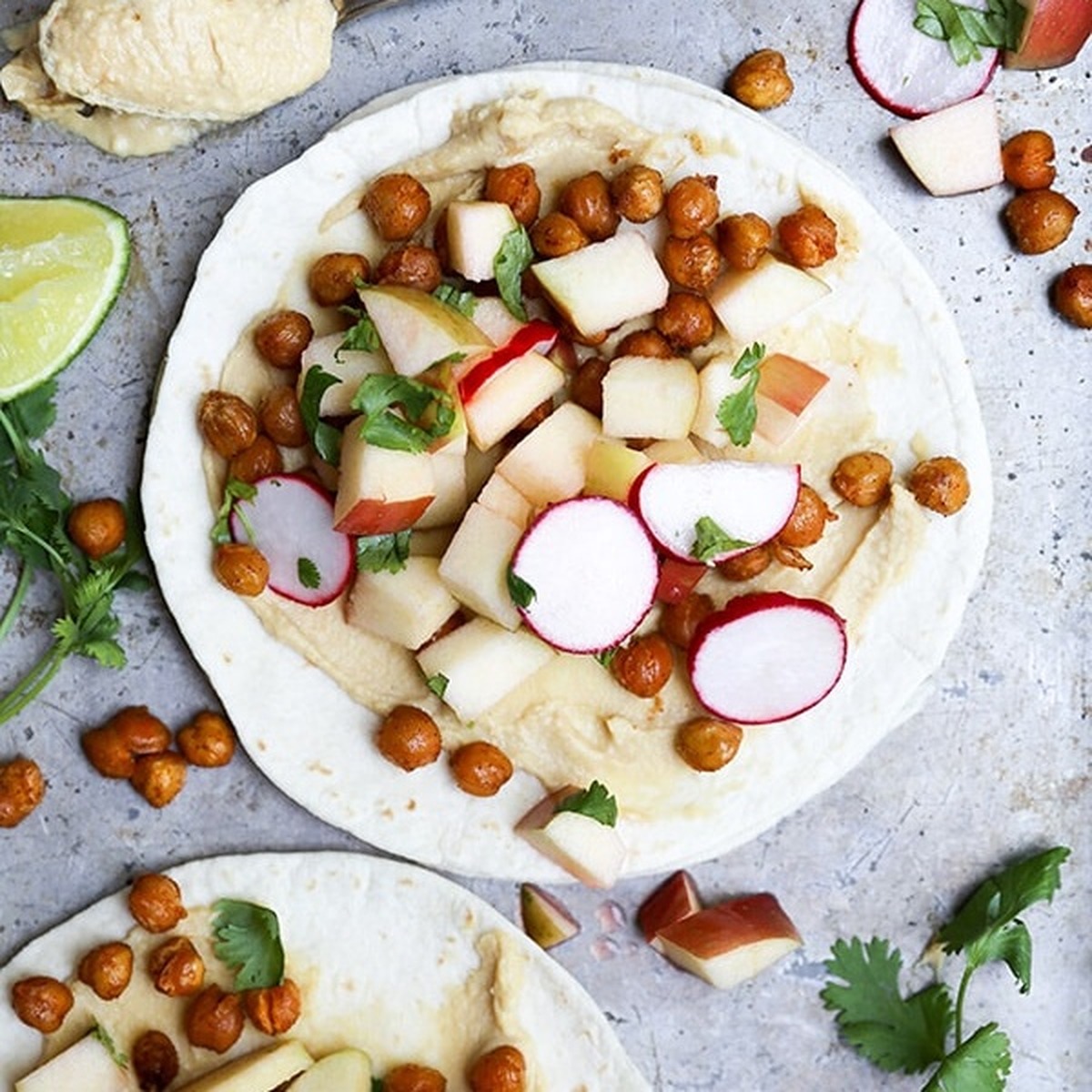 Overhead view of open-faced spiced chickpea tacos topped with crispy roasted chickpeas, diced apple, sliced radish, and cilantro on a baking sheet