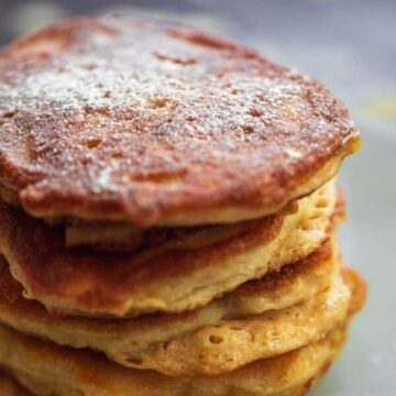 Stack of vegan apple pancakes (Oladyi) dusted with powdered sugar