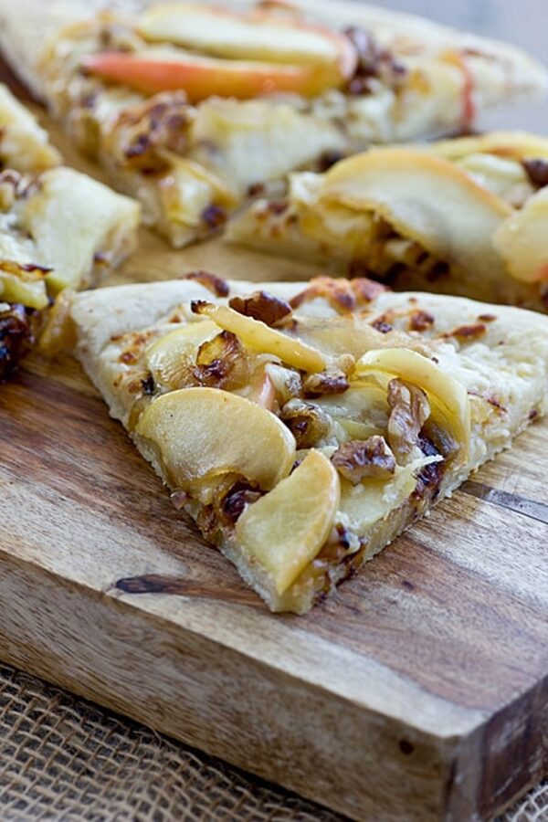 A slice of apple cheddar pizza with caramelized onions and walnuts on a wooden cutting board