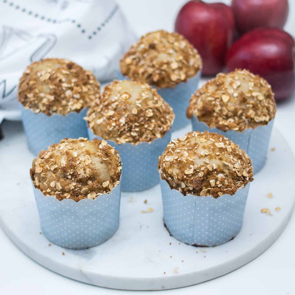 Apple and cottage cheese muffins with oat streusel on a white marble board, with red apples behind