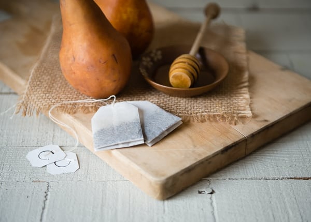 Bosc pears, chai tea bags and a honey dipper on a wooden cutting board