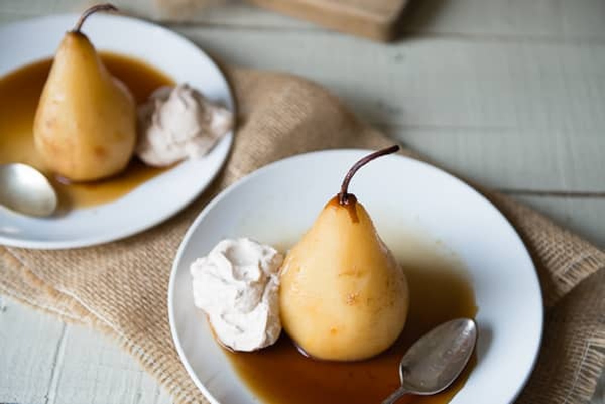 Two white plates of chai poached pears with cinnamon whipped cream and spoons on a burlap cloth