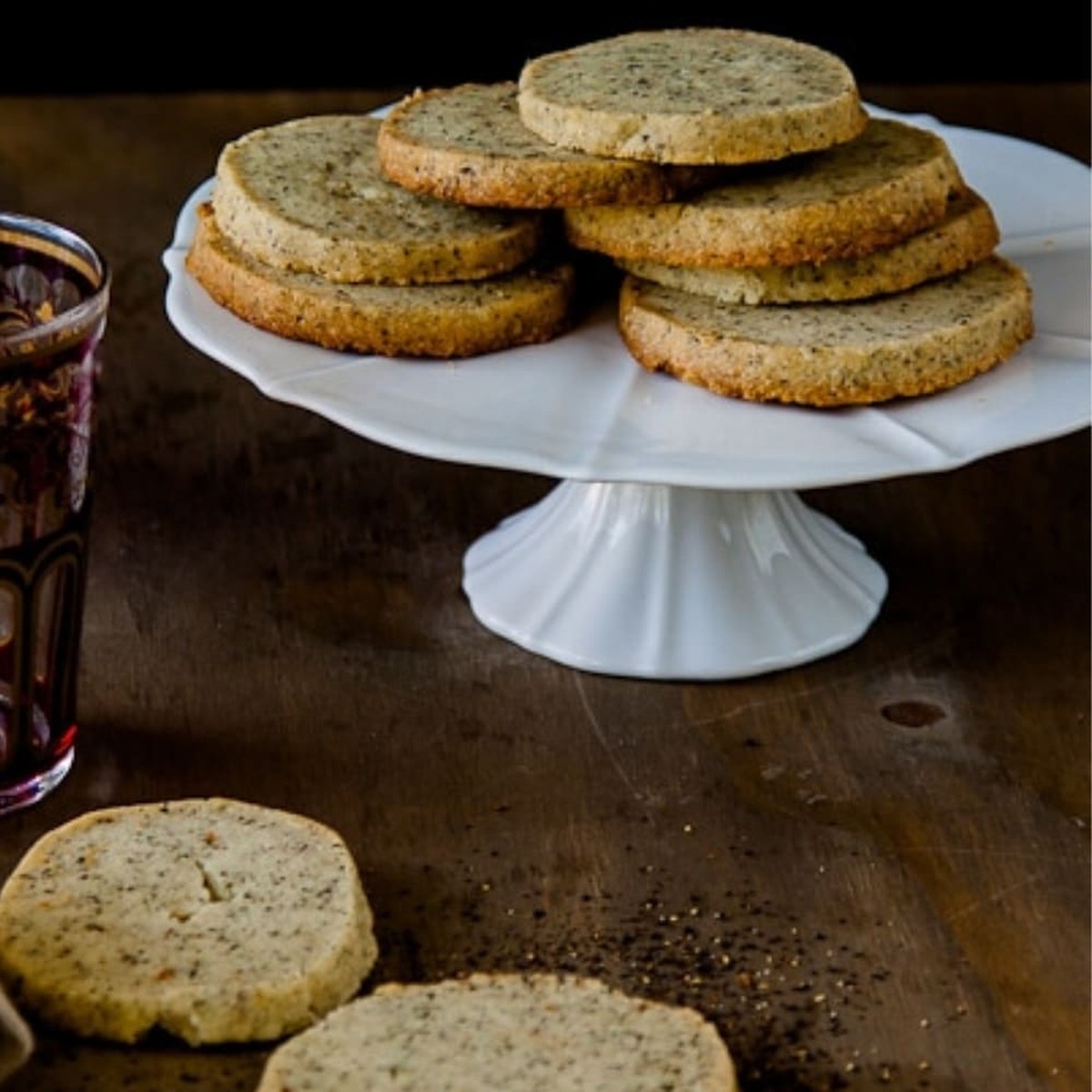 Chai shortbread cookies stacked on a white cake stand with a glass of tea